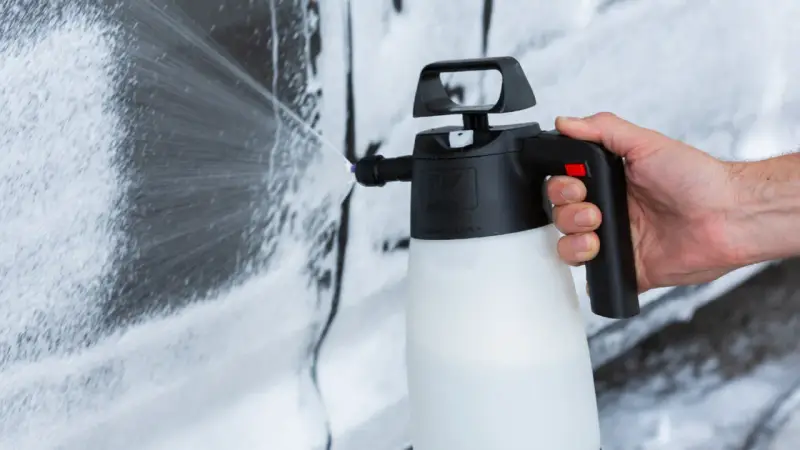 Mano che spruzza schiuma per lavare auto a casa con un erogatore.