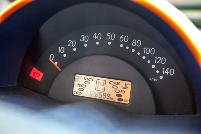 Cruscotto auto con tachimetro e spia del freno di stazionamento accesa. Chilometraggio 122599 km.